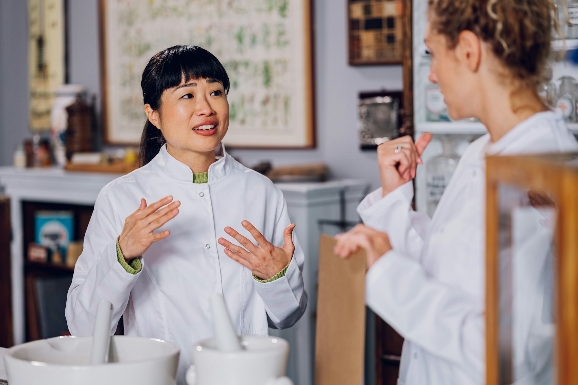 A Japanese chemist is standing with her assistant in the pharmacy